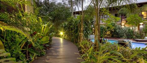 A wooden pathway surrounded by lush greenery leading to a pool area.