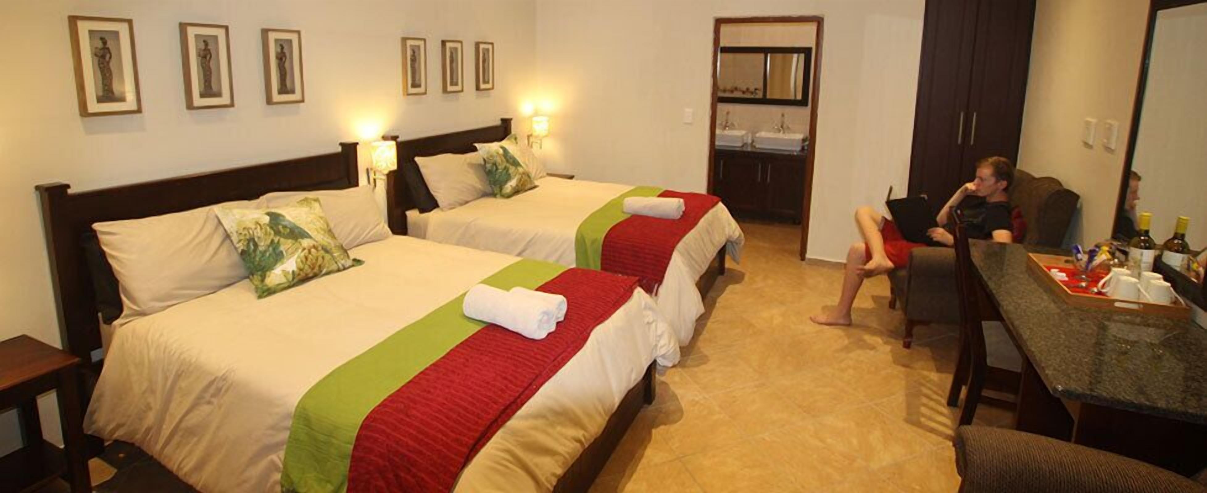 A hotel room with two beds, a desk, and a mirror.