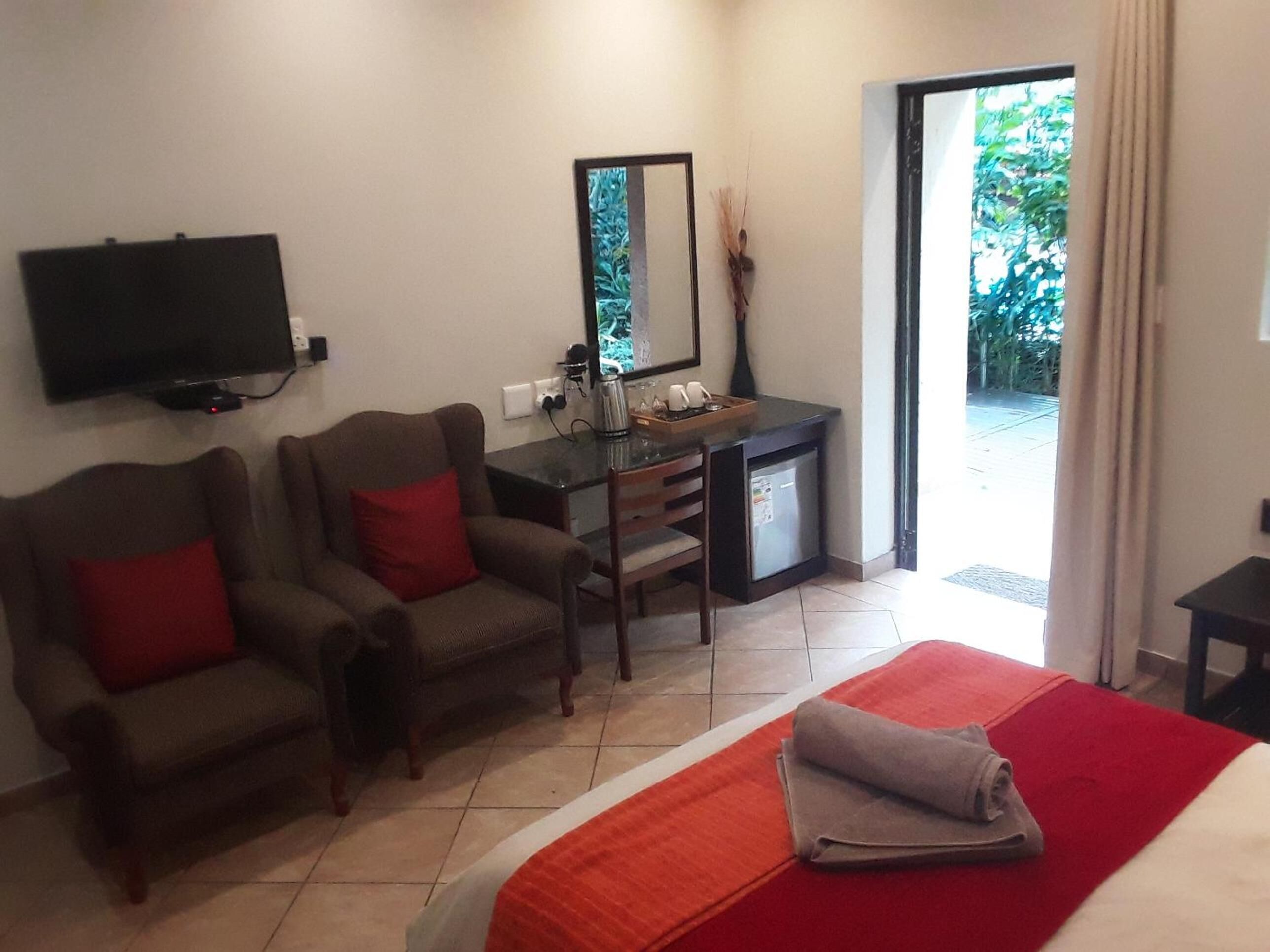 Hotelkamer met een bed, twee fauteuils, een bureau met een computer, een televisie en een schuifdeur naar buiten.