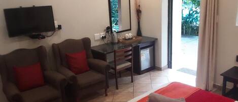 Hotelkamer met een bed, twee fauteuils, een bureau met een computer, een televisie en een schuifdeur naar buiten.