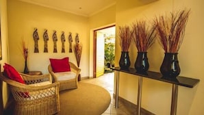 A hallway with wicker furniture, a red pillow, and vases with tall plants. - Forest Villas (St. Lucia)