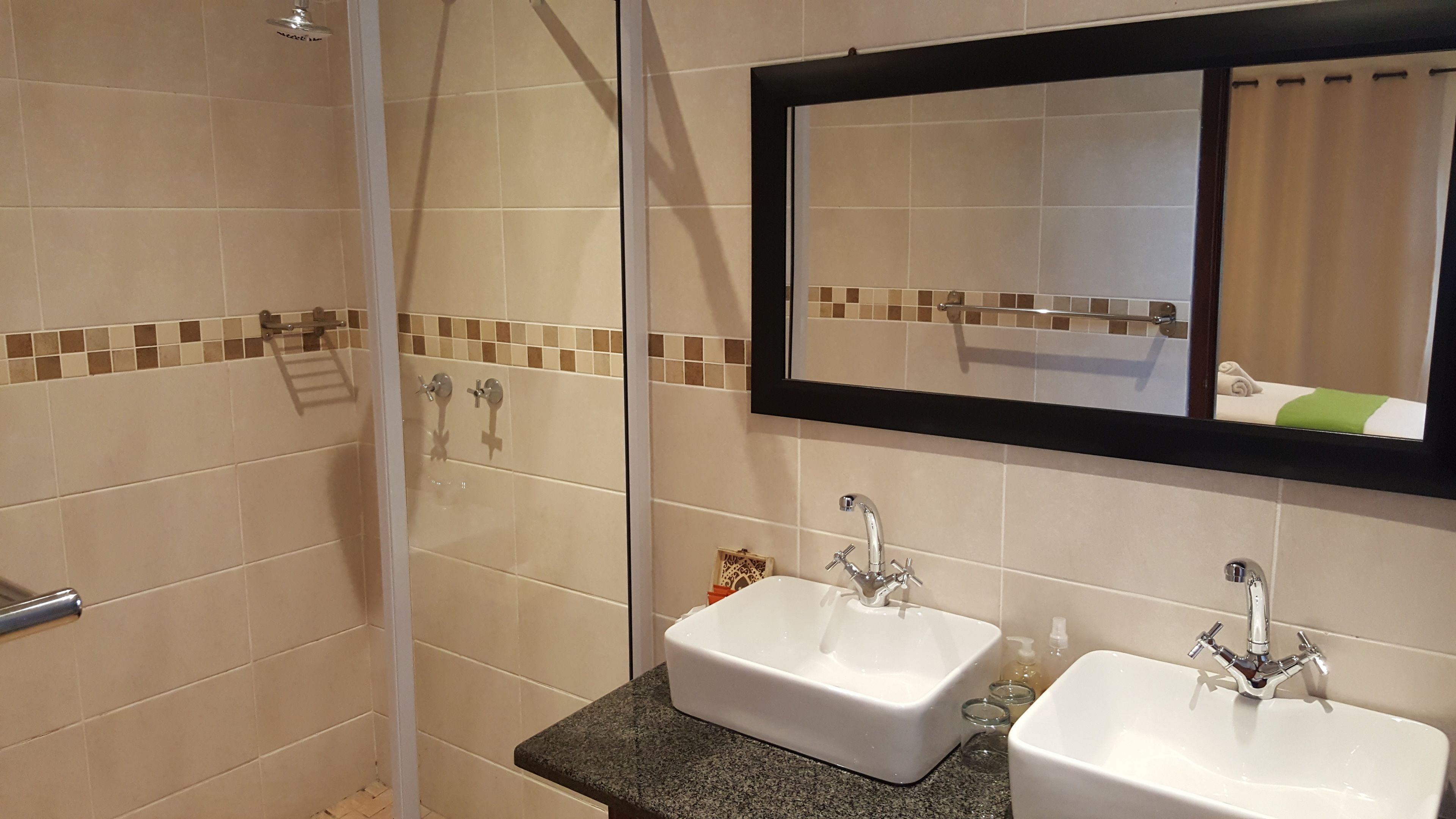 A bathroom with two sinks, a shower, and a mirror.