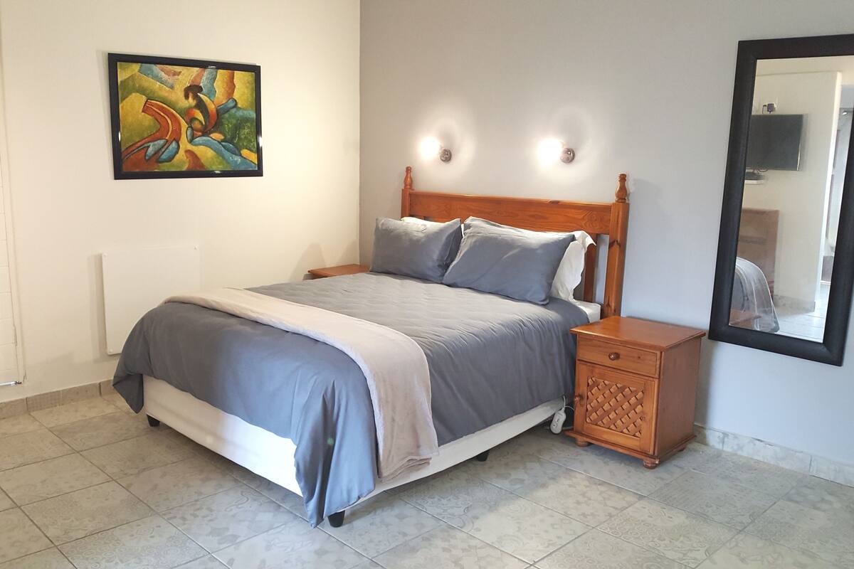 Une chambre à coucher comprenant un lit, une table de chevet, des lampes fixées au mur, un tableau et un miroir.