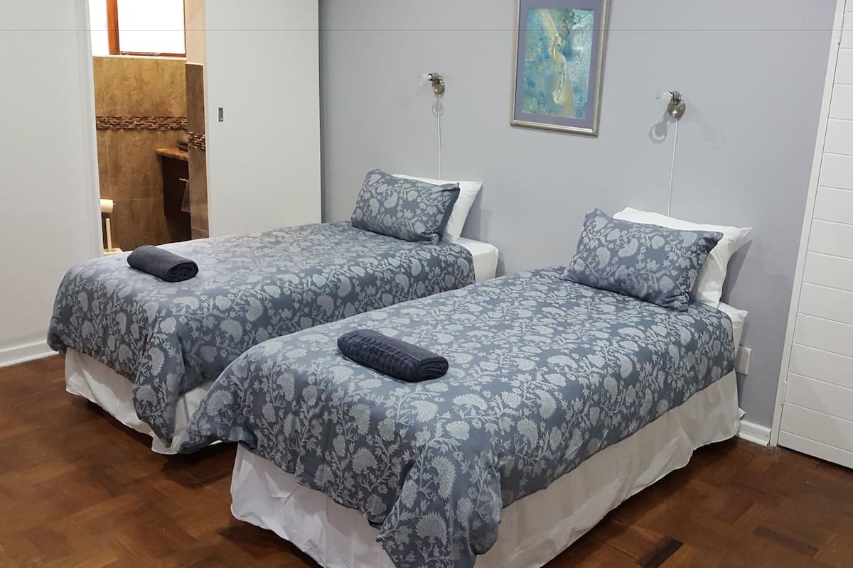 Une chambre avec deux lits, chacun recouvert d’une couvre-lit et agrémenté d’oreillers à motifs floraux, un plancher en bois et un tableau accroché au mur.