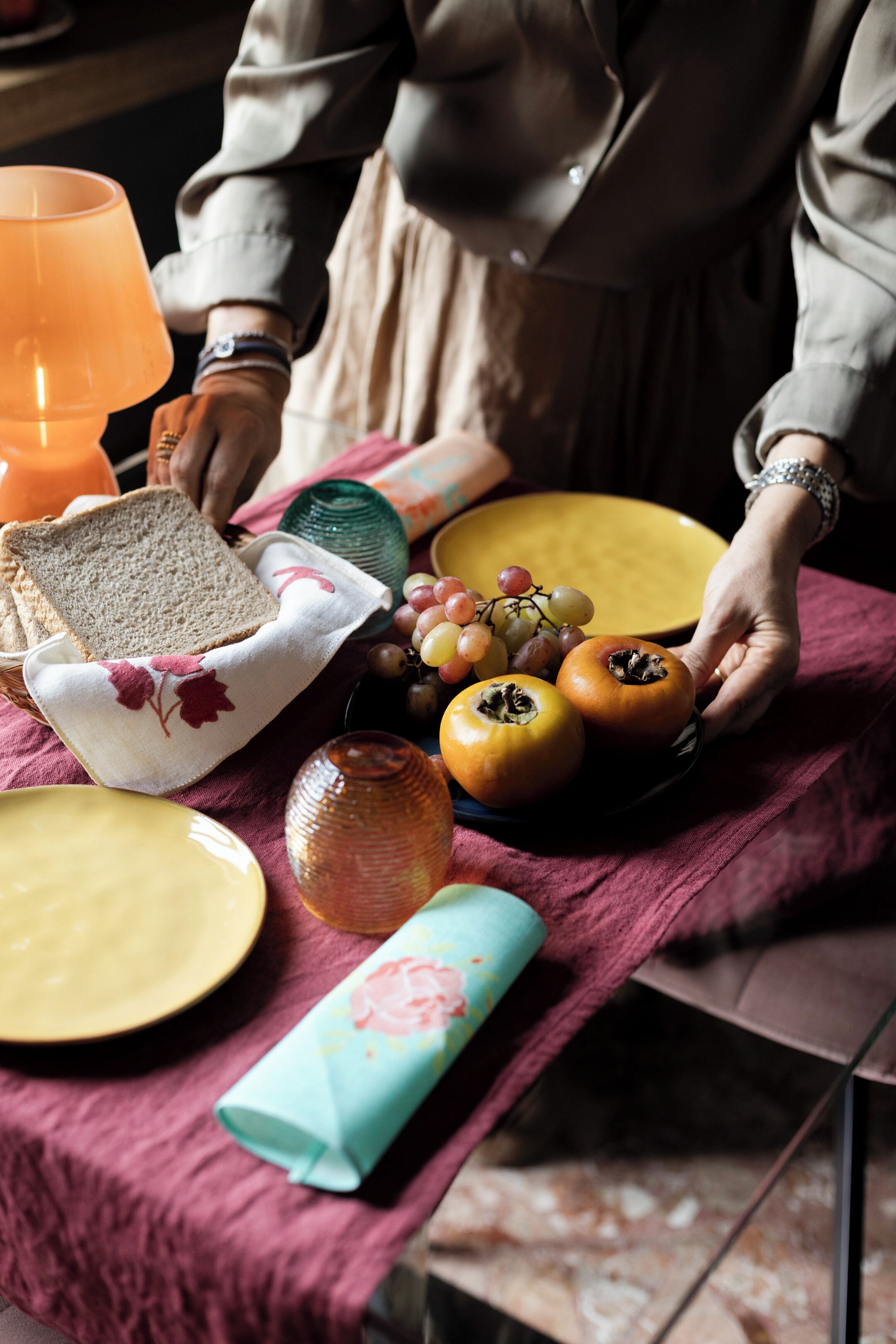 Une table avec du pain, des tomates, des raisins et un verre de jus d’orange.