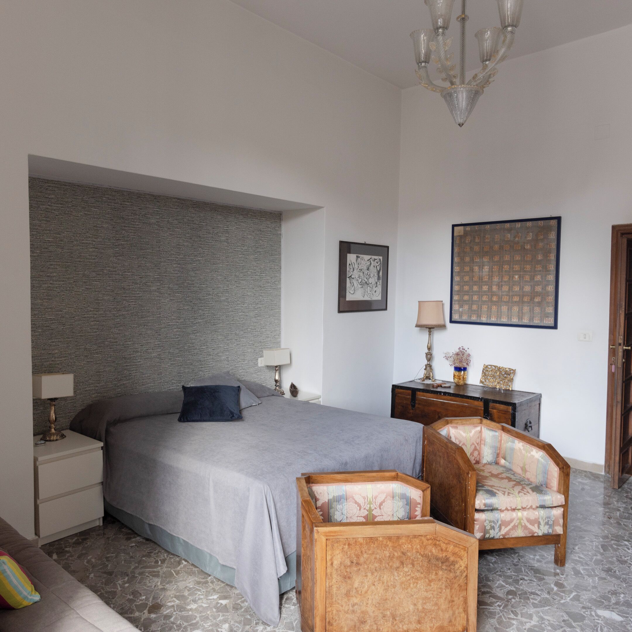 Un dormitorio con cama, mesitas de noche, cómoda, silla, lámpara y candelabro.