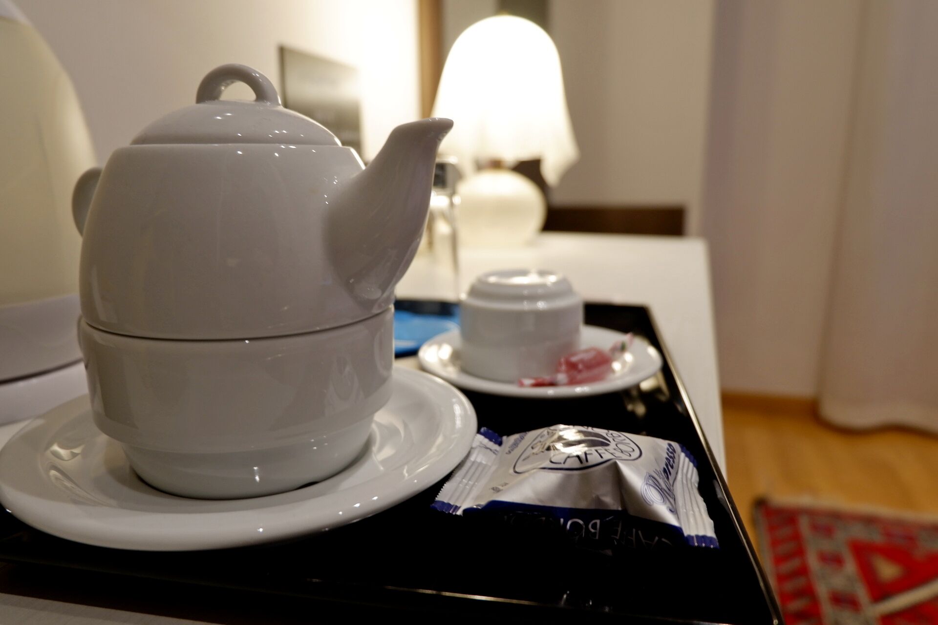 A white teapot on a tray with a white cup and a packet of coffee creamer.