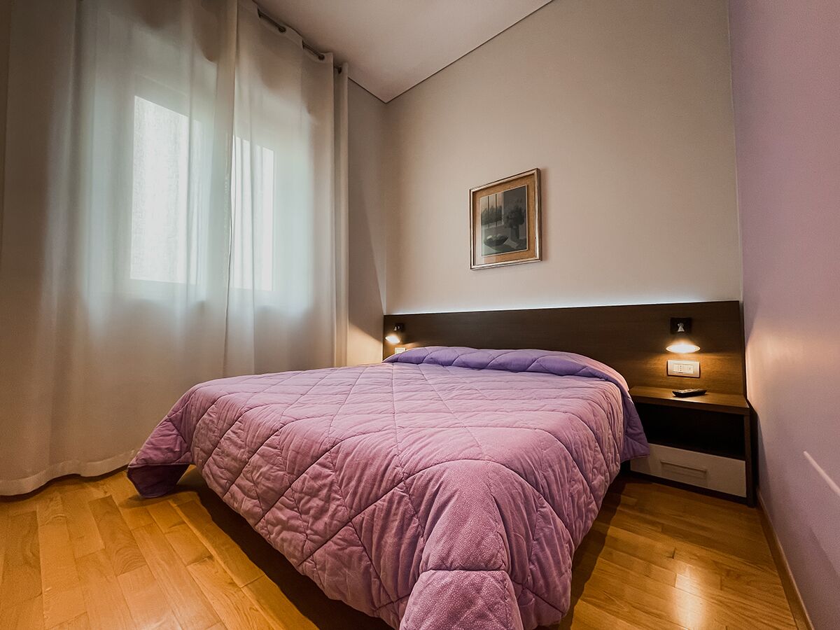 Quarto com cama, mesa de cabeceira, luminária, pintura na parede e janela com cortinas.