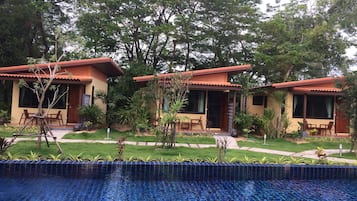 Zona de piscina con bordeado de azulejos, rodeada por un pequeño jardín con plantas y una estructura de madera.