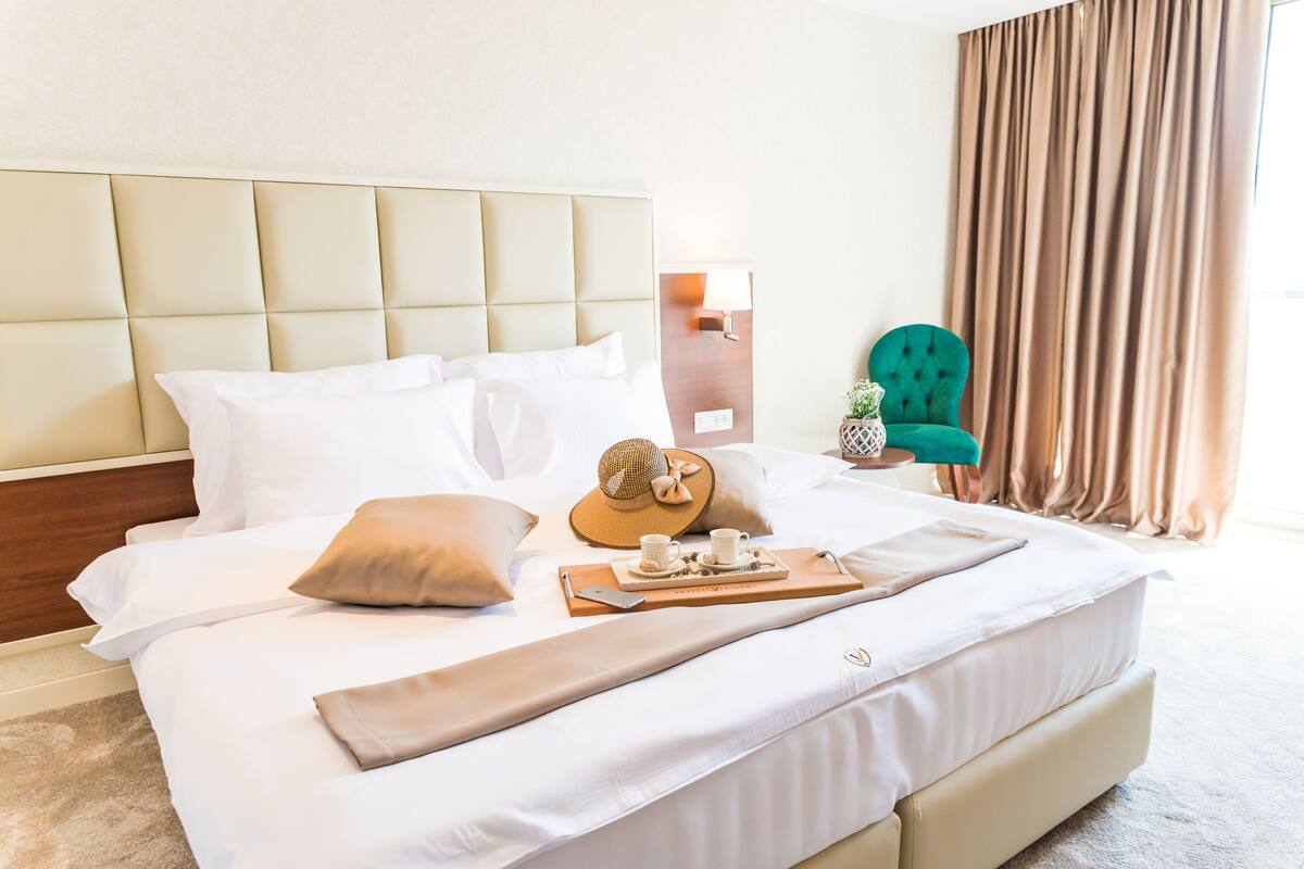 A neatly made bed with white linens, a wooden headboard, and a tray with a hat and two cups.