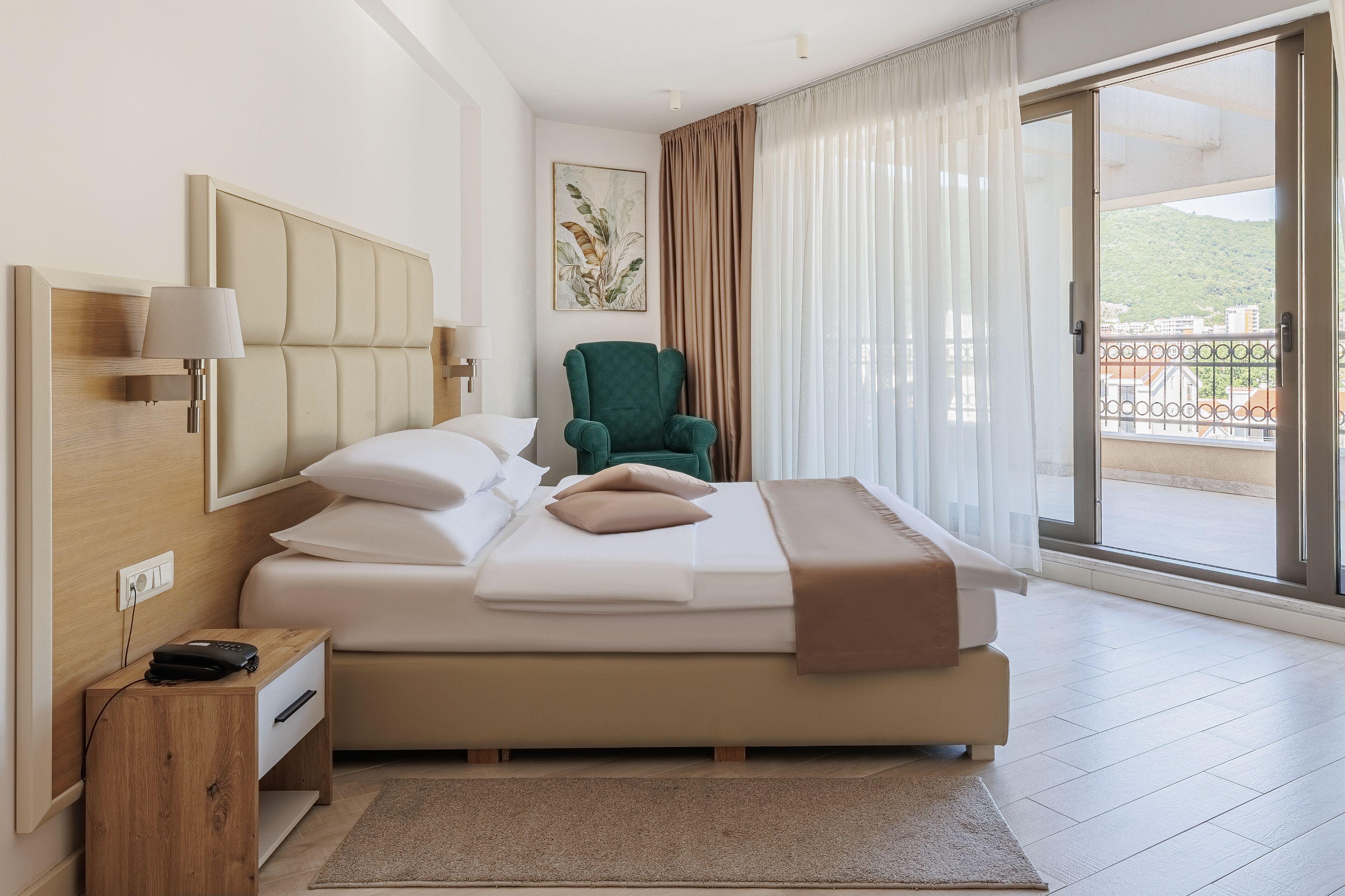 Quarto moderno com cama, mesa de cabeceira, uma cadeira e uma janela grande com cortinas.