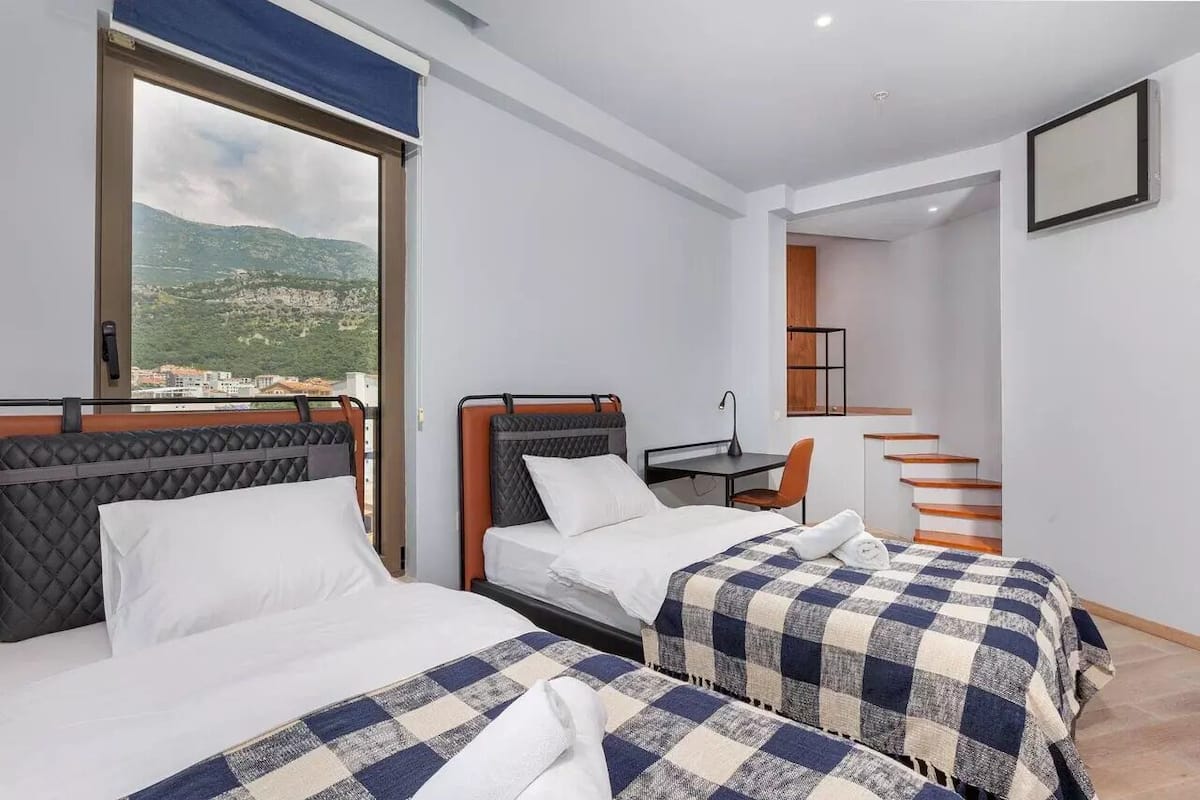 A hotel room with two beds, a desk, and a staircase.