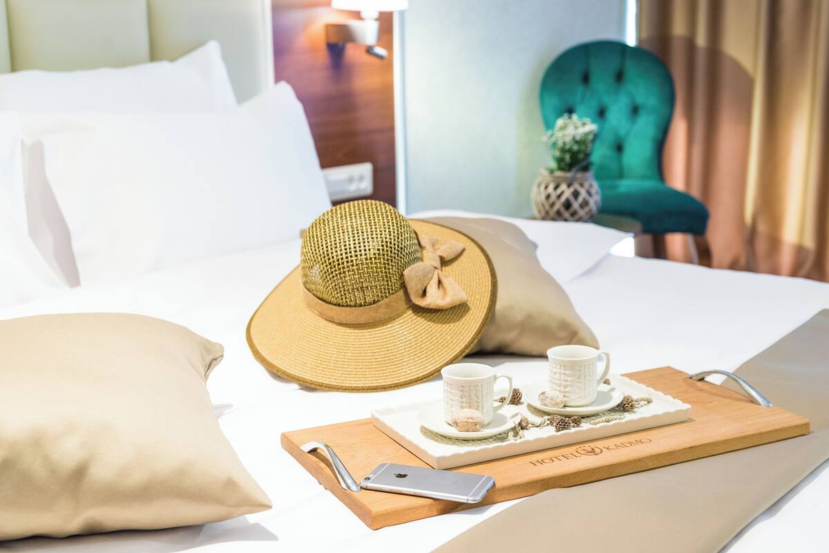 A neatly made bed with a straw hat, two white cups, and a tray with cookies.