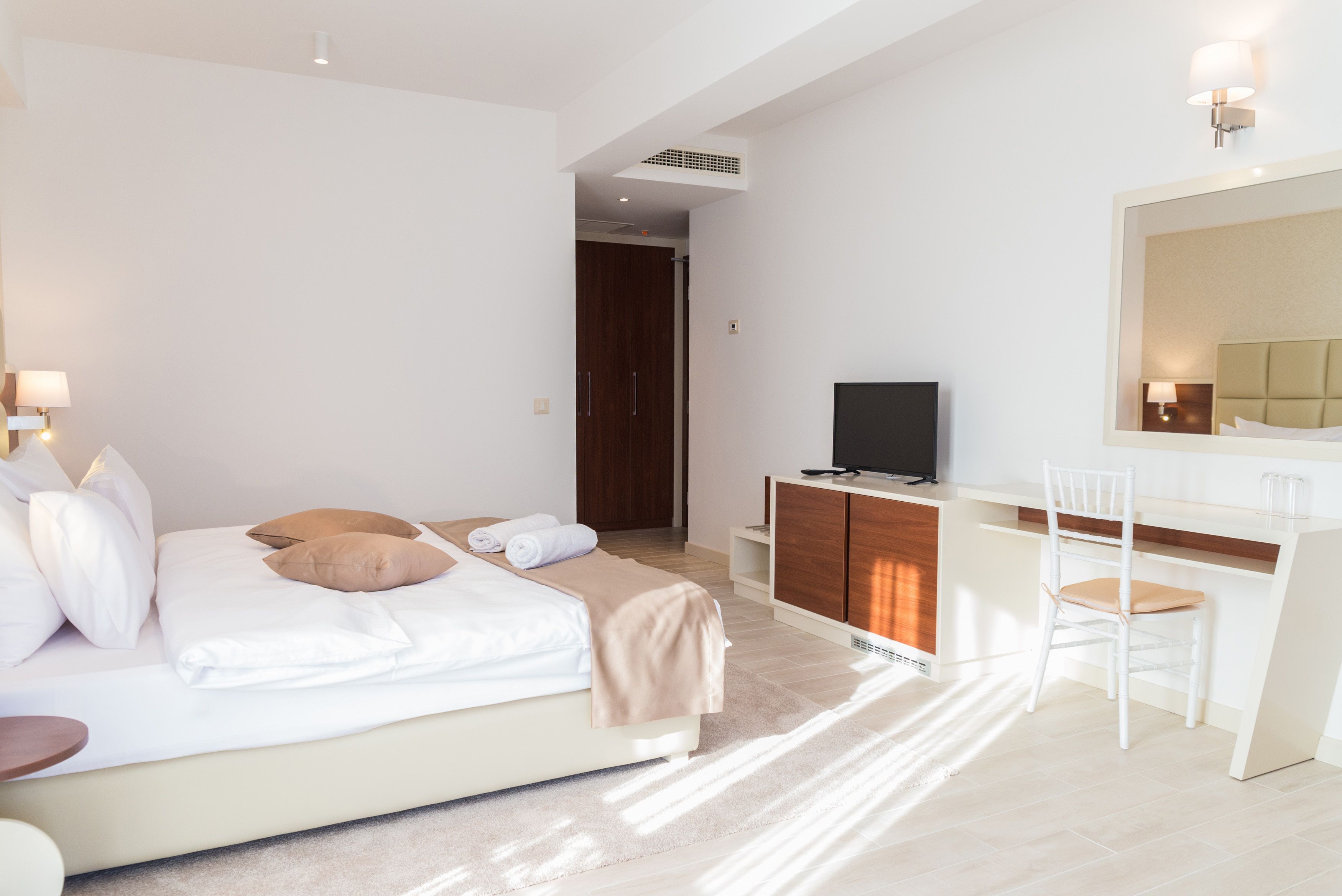 A modern hotel room with a bed, a desk, a chair, a TV, and a mirror.