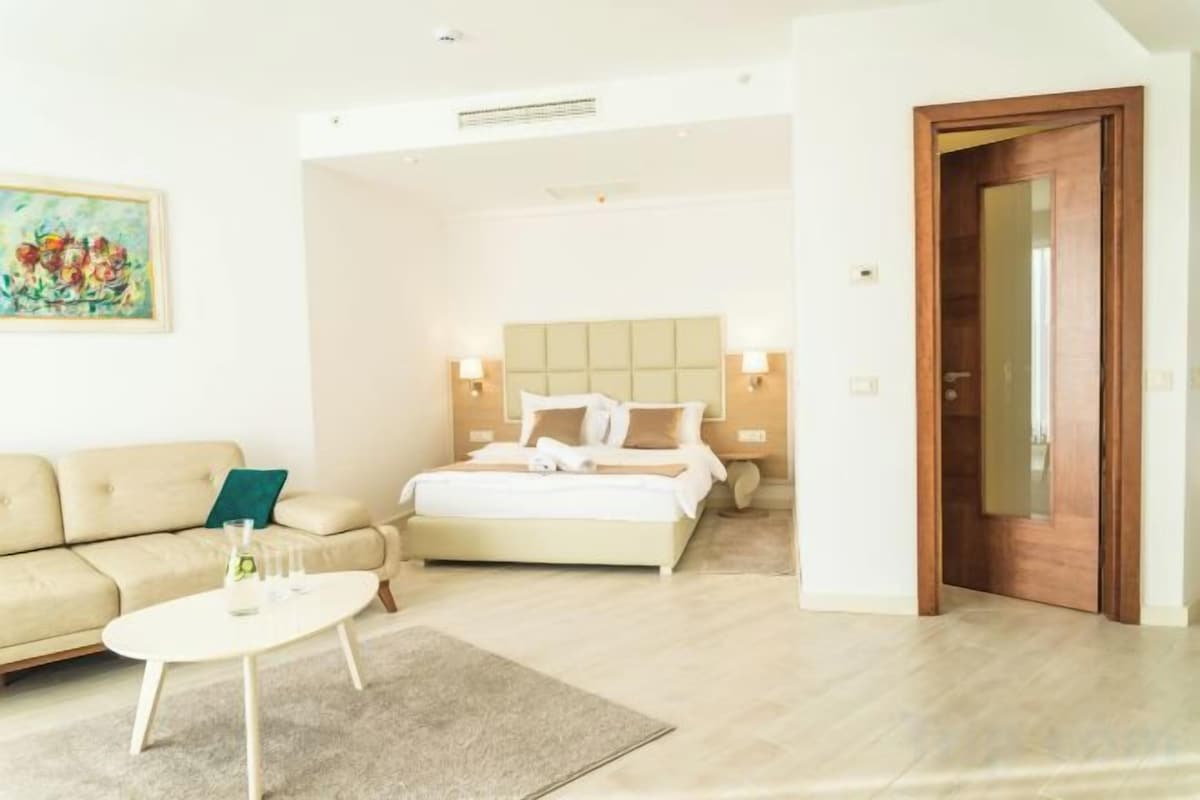 A hotel room with a bed, a sofa, a coffee table, and a painting on the wall.