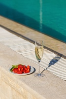 Una copa de vino blanco junto a un plato de fresas en el borde de una piscina.