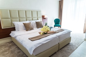 A hotel room with a large bed, a headboard, a wooden nightstand, a teal armchair, and a window with curtains. - Hotel Kadmo by Aycon (Budva)