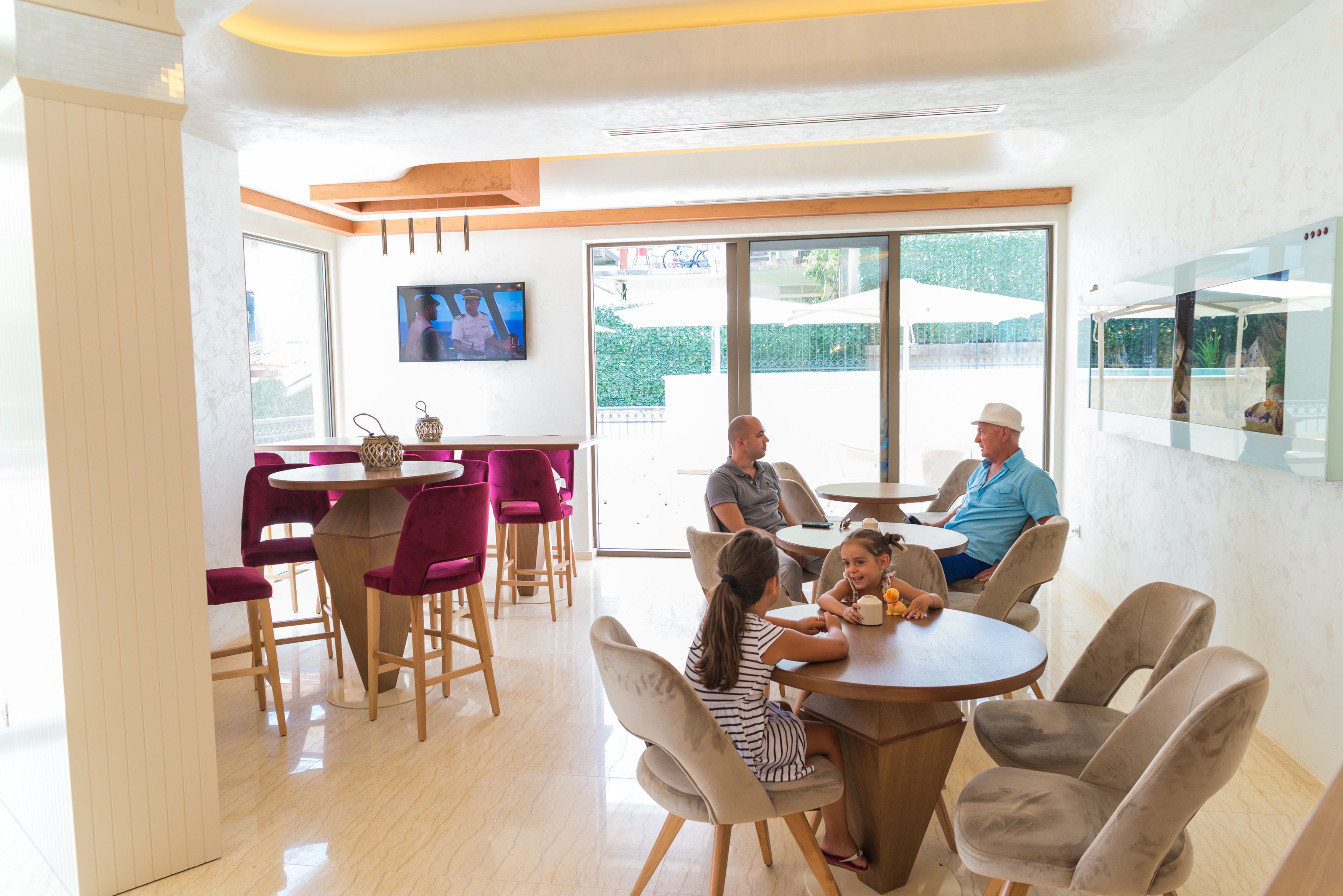 A modern dining area with round tables and chairs, a TV mounted on the wall, and large windows providing a view of the outdoors.