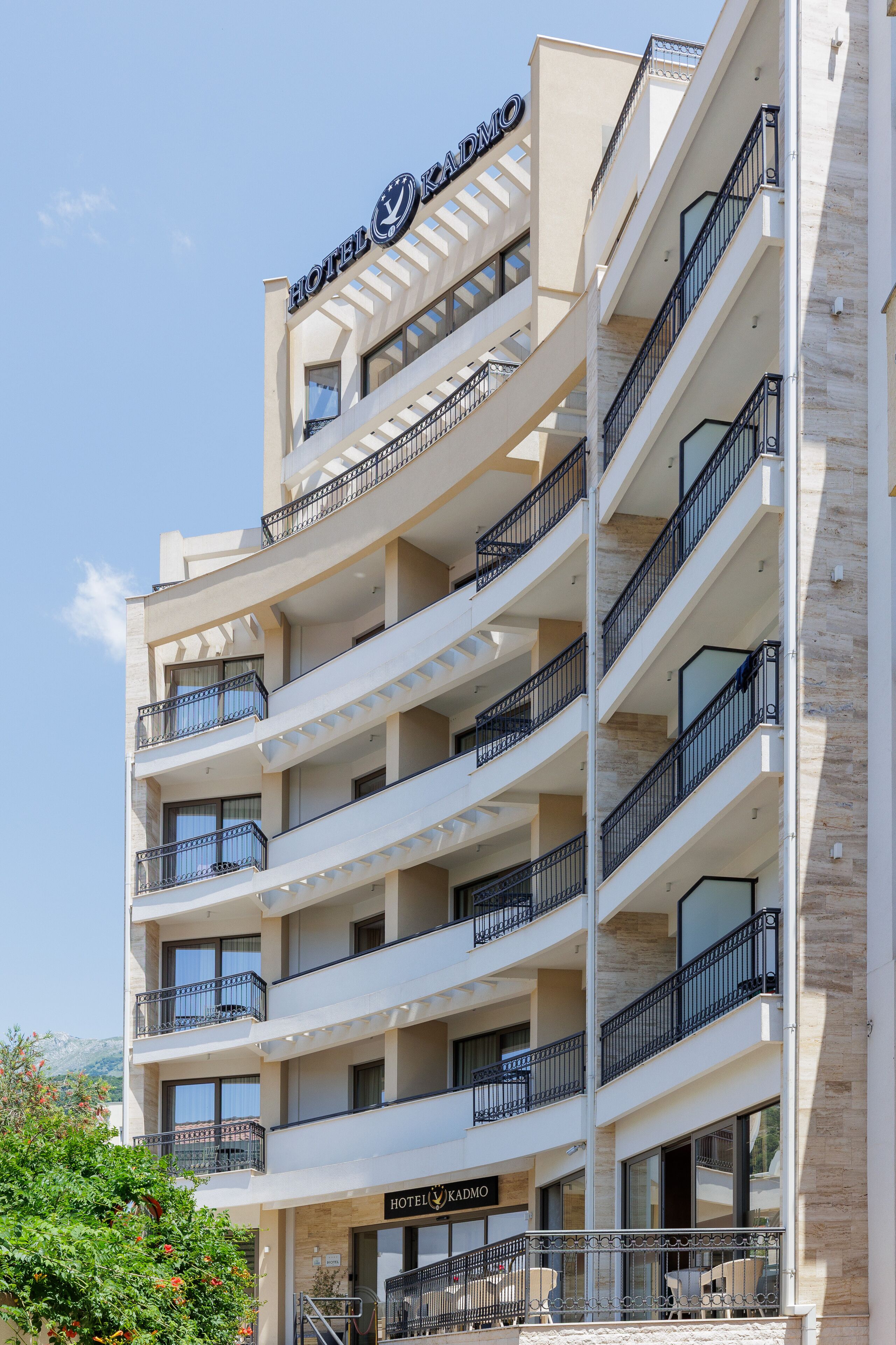A multi-story hotel with balconies, a sign reading "HOTEL KADMO," and a clear sky.