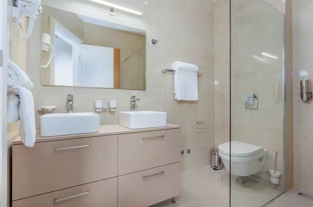 A modern bathroom with two sinks, a large mirror, a glass shower enclosure, and a toilet.