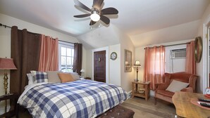 A bedroom with a bed, a wooden bench, a desk, a chair, a ceiling fan, and a window with curtains. - The Inn (Gravenhurst)