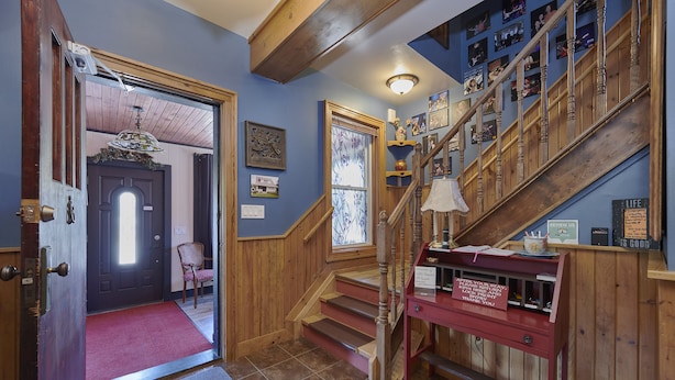 A wooden staircase with a red bench, a door with a red carpet, and a wall with framed pictures. - The Inn (Gravenhurst)