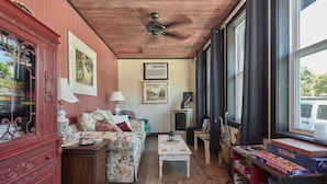 A cozy living room with a wooden ceiling, a floral sofa, a white coffee table, and a bookshelf filled with books. - The Inn (Gravenhurst)