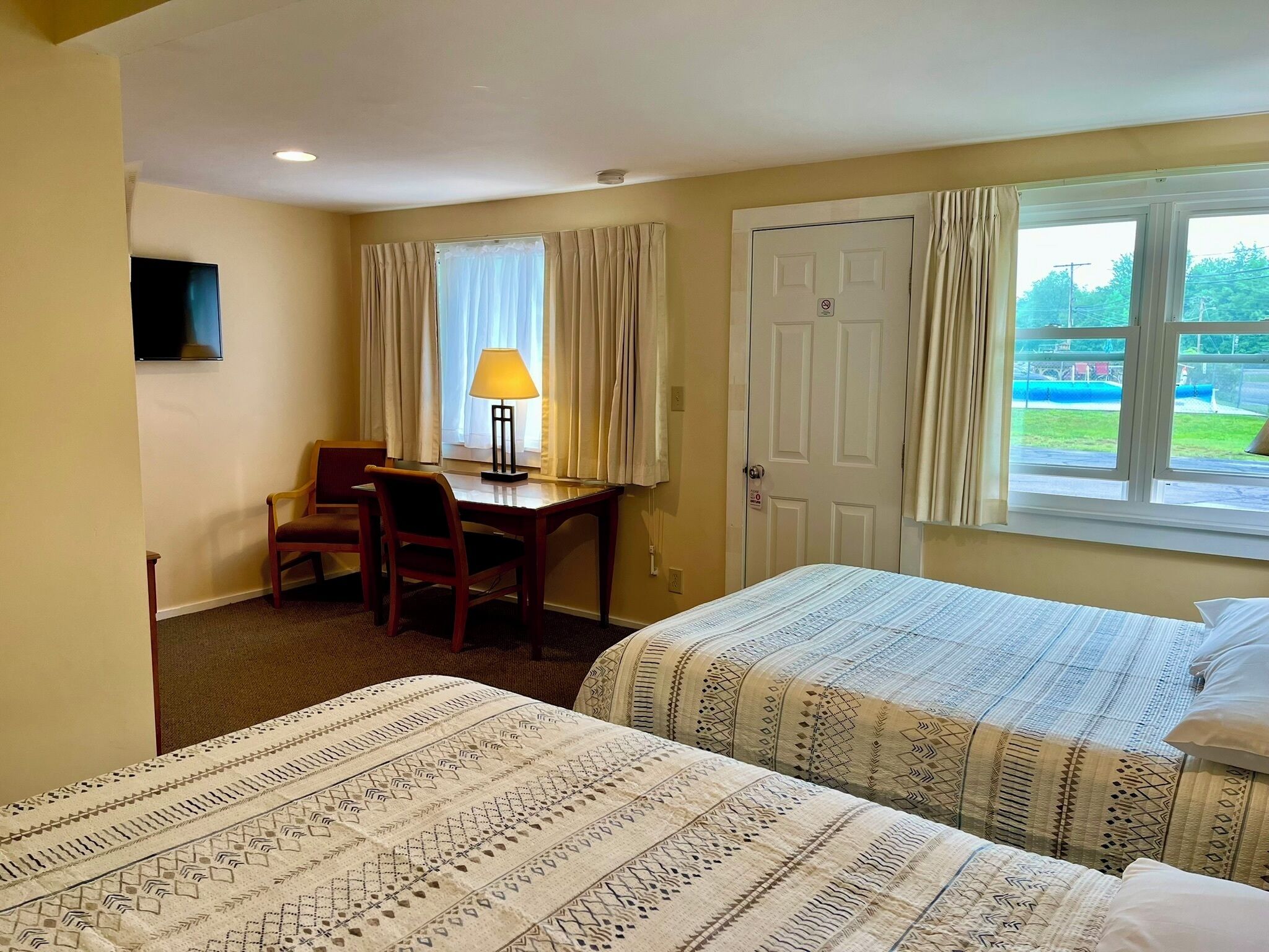 A hotel room with two beds, a desk with a chair, a lamp, and a window with curtains.