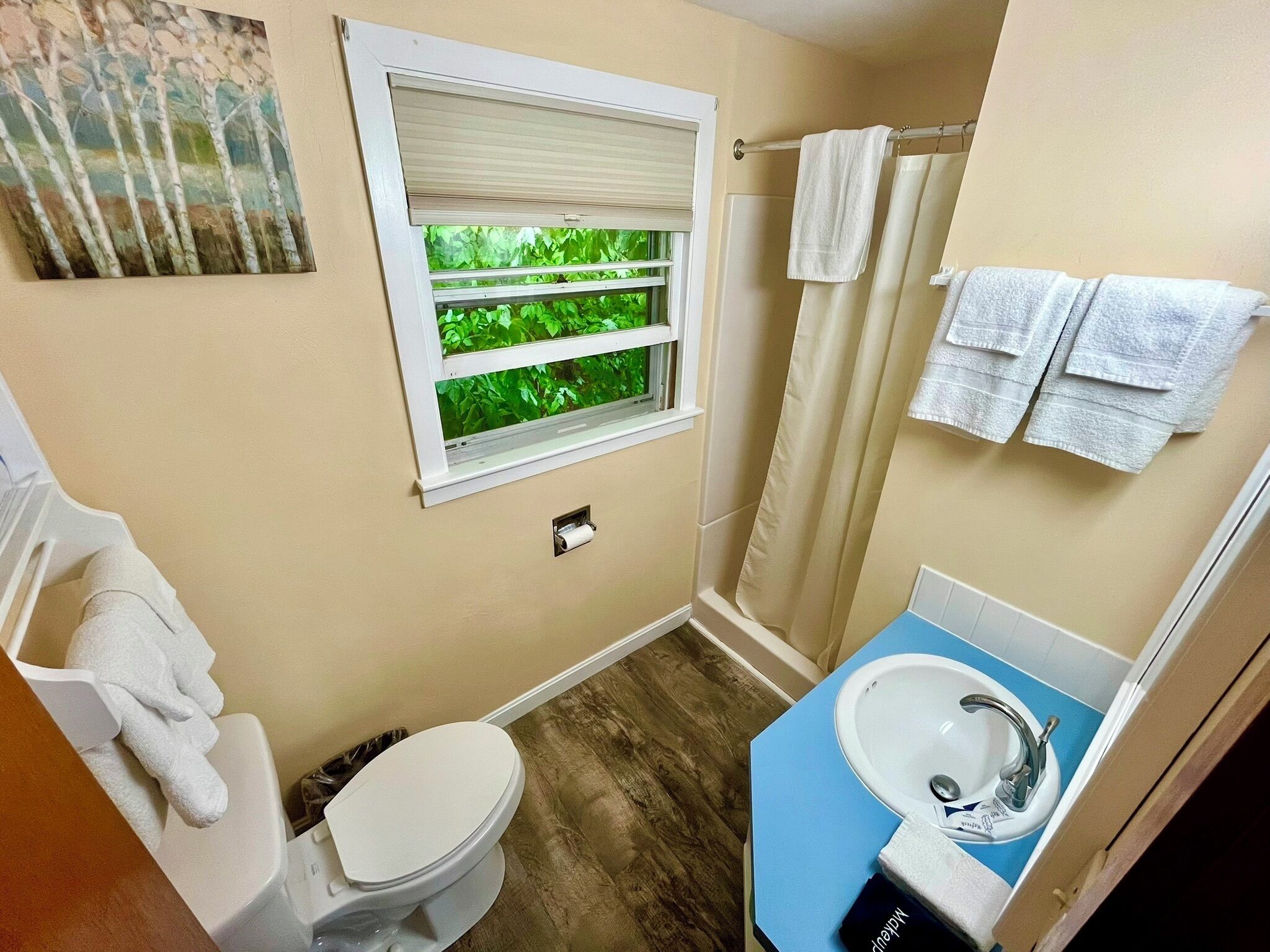 Et badeværelse med toilet, vask, vindue med skodder og bruseforhæng.