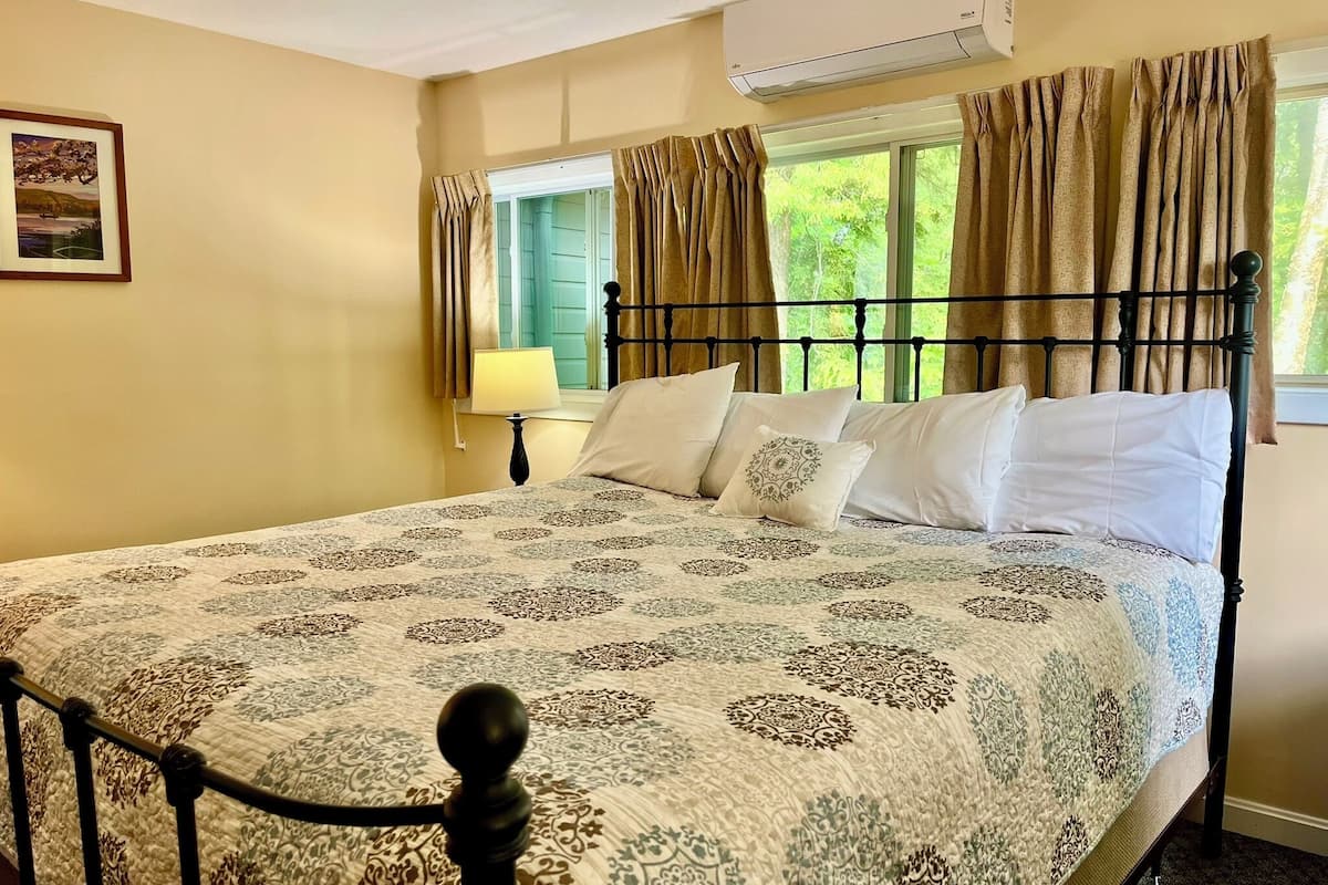 A neatly made bed with a patterned bedspread, a bedside lamp, and a window with curtains.