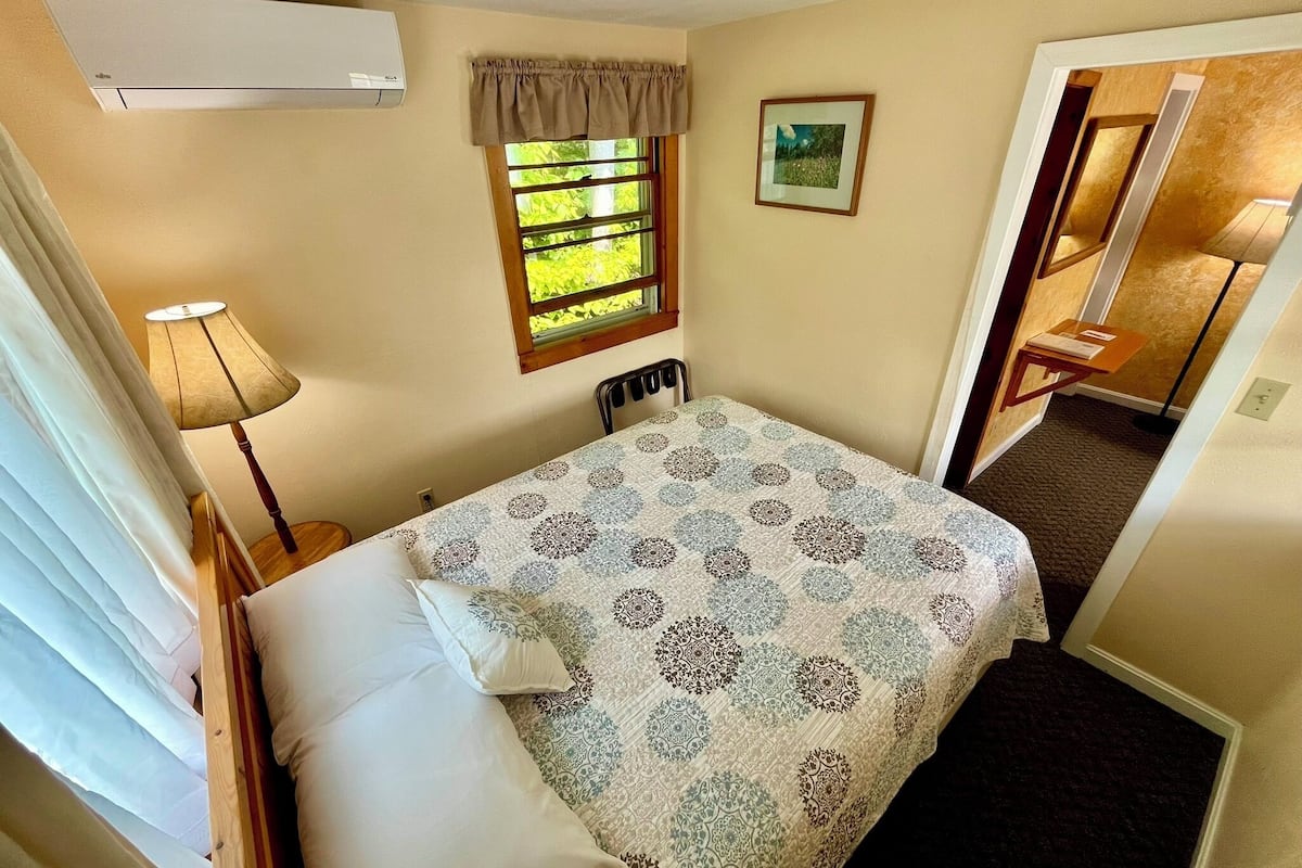 A bedroom with a bed, a window with curtains, a lamp, and a picture on the wall.