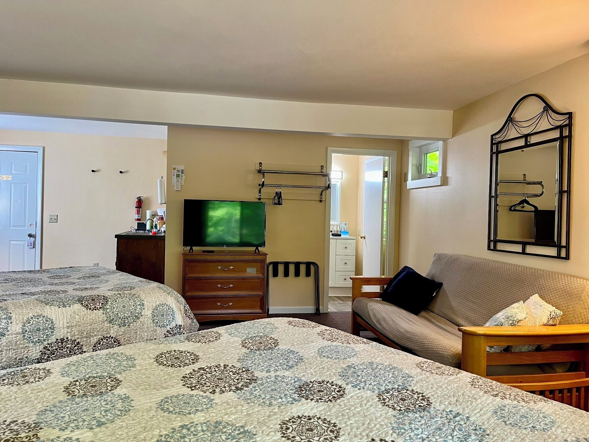A hotel room with two beds, a TV, a dresser, a sofa, and a mirror.