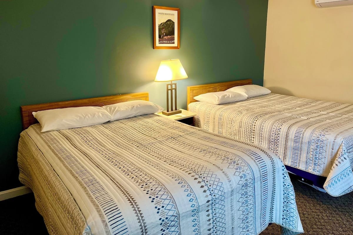 A hotel room with two beds, each with a patterned bedspread, a nightstand with a lamp, and a framed picture on the wall.
