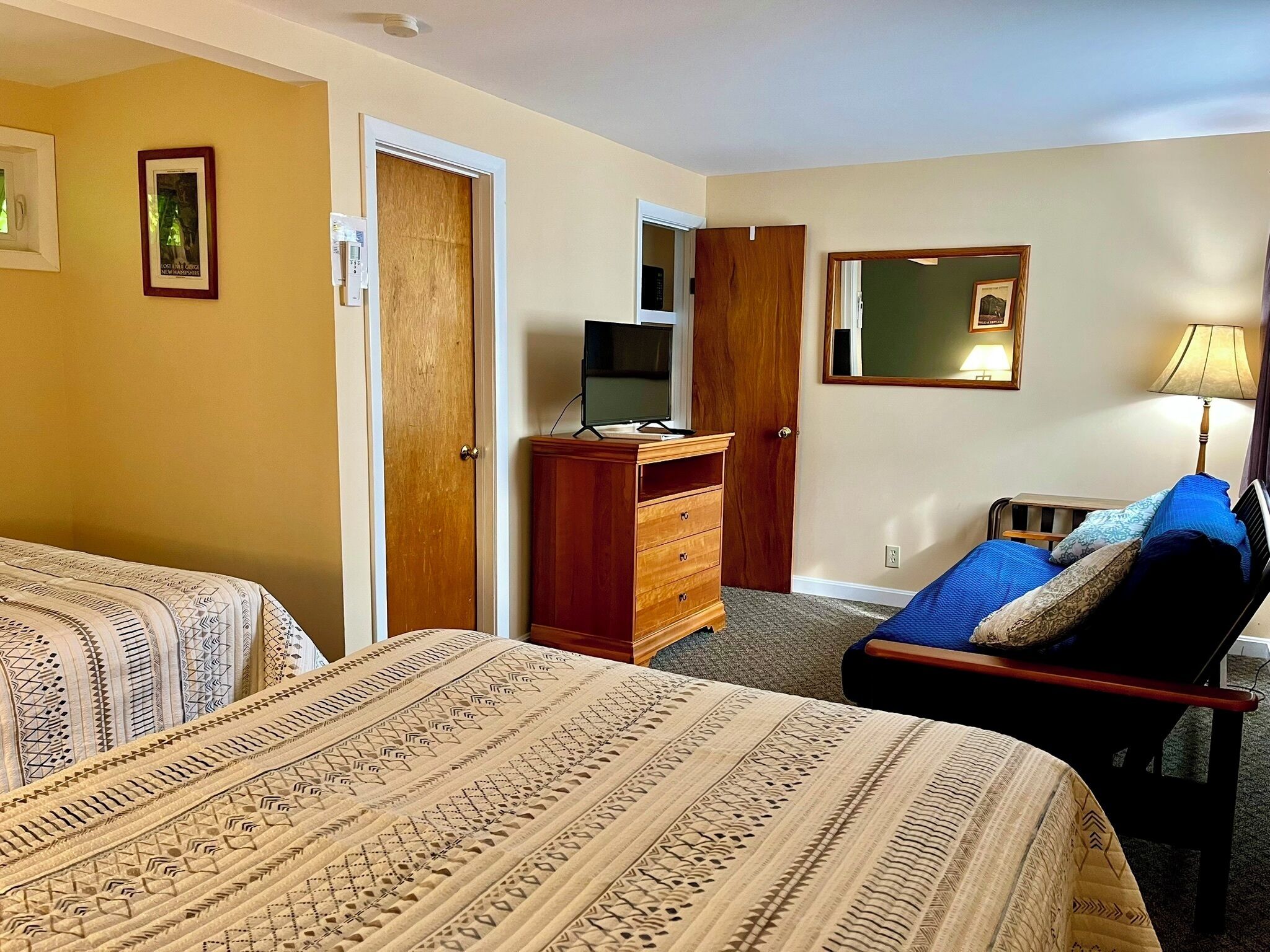 Ett hotellrum med två sängar, en byrå i trä, en tv och en spegel.