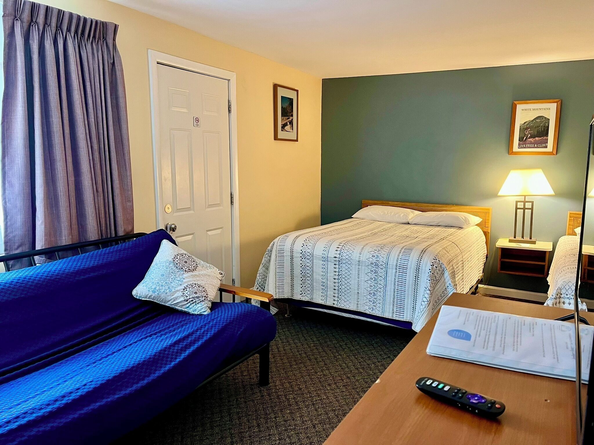 A hotel room with a bed, a sofa, a desk with a remote control, and a lamp.