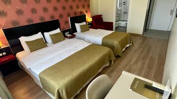 A hotel room with two beds, a desk, a chair, a red chair, a shower, and a door.