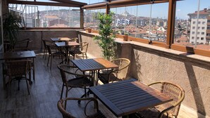 A rooftop terrace with wooden tables and wicker chairs, offering a view of a cityscape with buildings and a mosque. - Era Palace Hotel (Istanbul)