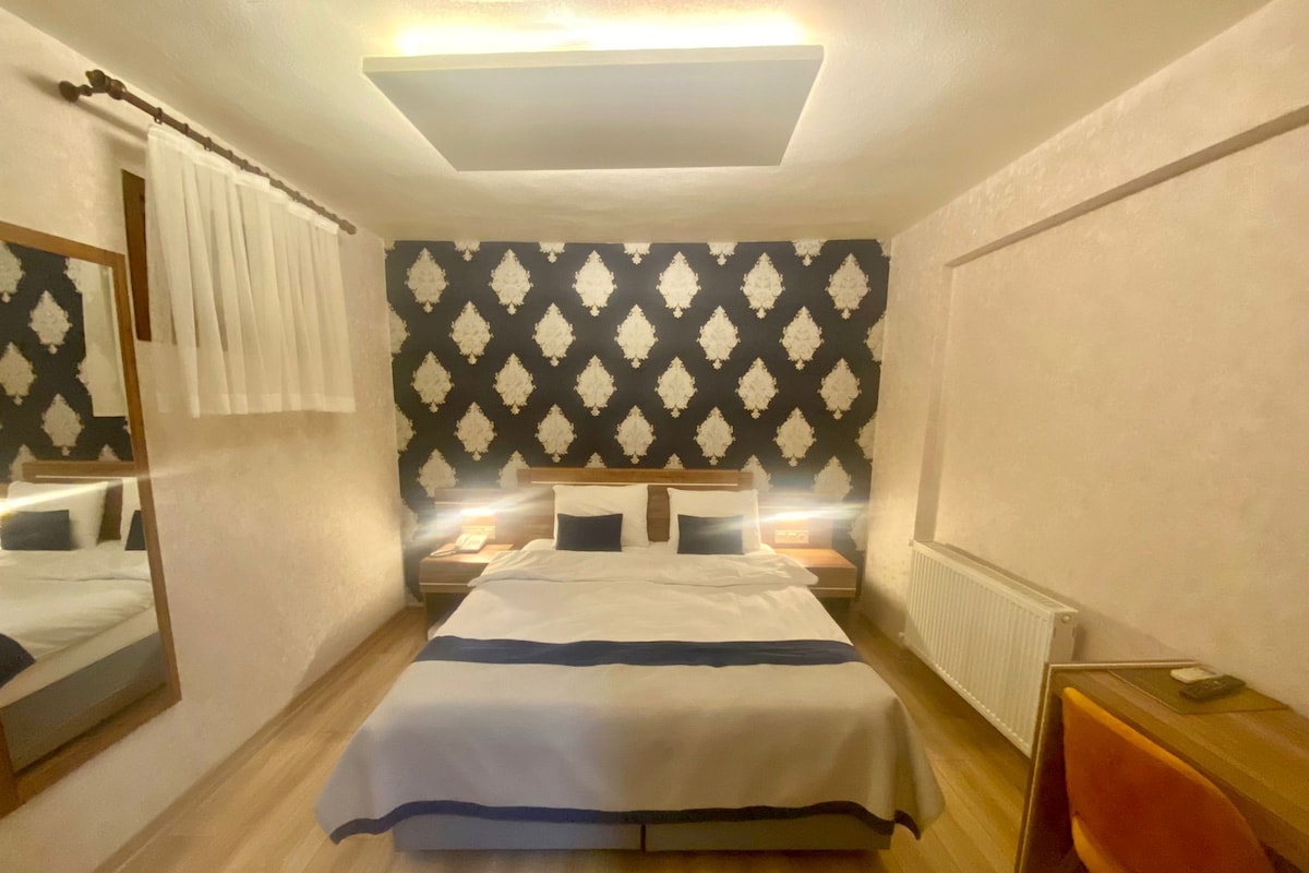 Habitación de hotel con una cama grande, mesitas de noche, un espejo, un radiador y suelo de madera.