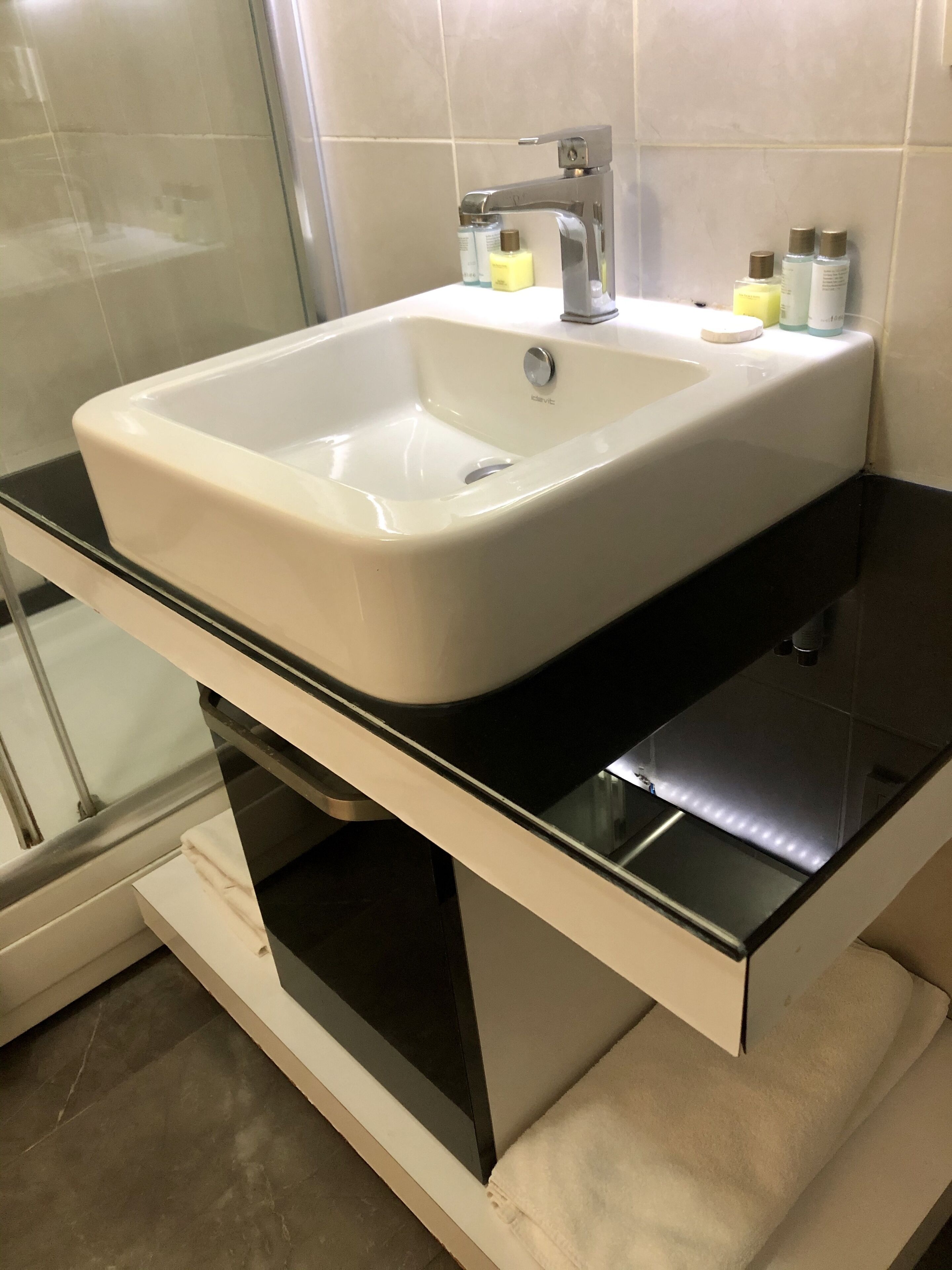 Un baño con lavamanos blanco, encimera negra y cabina de ducha de vidrio.