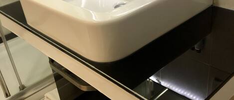 Un baño con lavamanos blanco, encimera negra y cabina de ducha de vidrio.