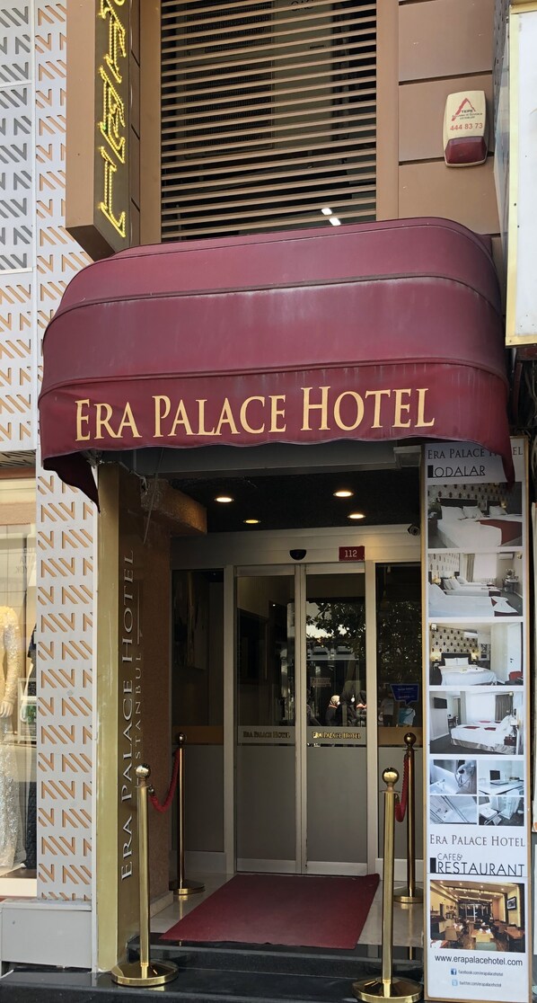 The entrance of Era Palace Hotel with a maroon awning and a glass door.