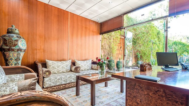 A modern living room with a wooden wall, a sofa with patterned cushions, a coffee table, and a large vase with flowers. - Hivernage Secret Suites & Garden (Marrakech)