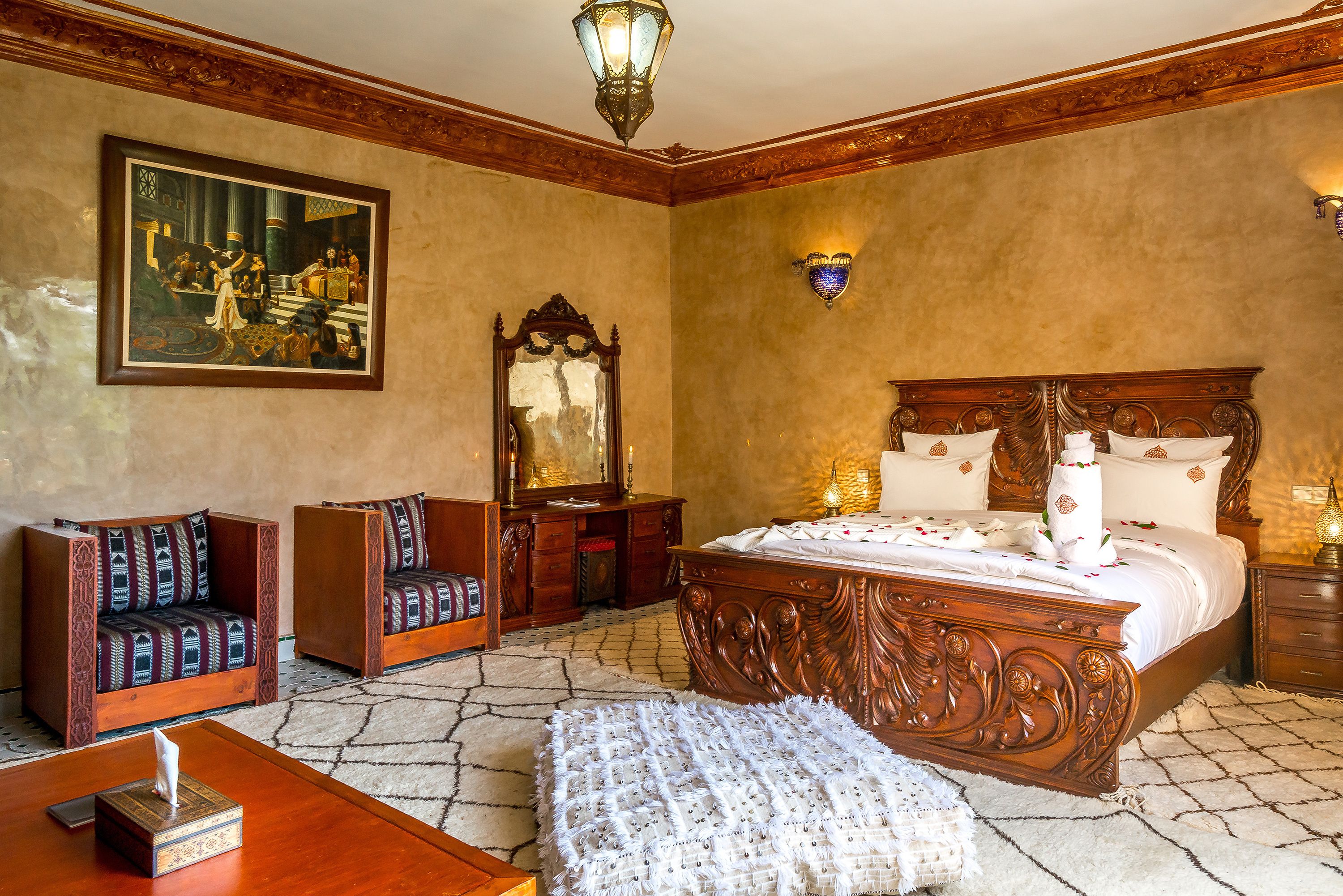 Une chambre à coucher avec un grand lit, deux fauteuils, une commode en bois, un miroir et un tableau accroché au mur.