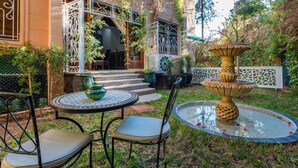 A courtyard with a fountain, a table with chairs, and a building with ornate metalwork.