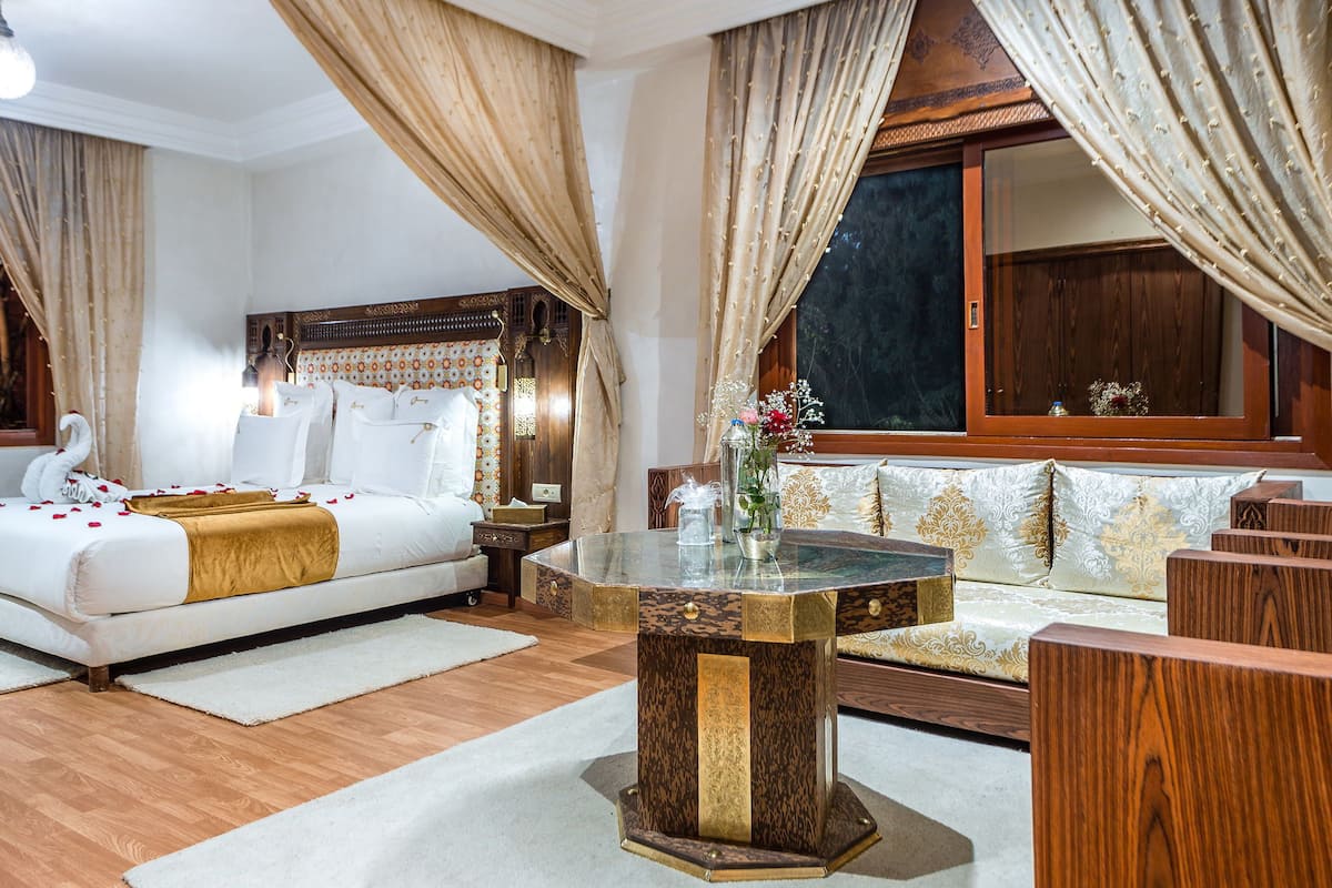 A hotel room with a bed, a glass coffee table, a sofa, and a large window with curtains.