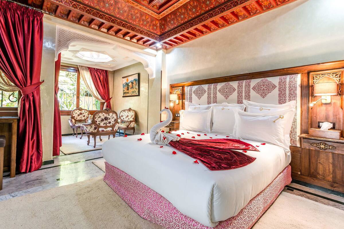 A spacious bedroom with a large bed, ornate headboard, and a chandelier.