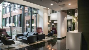 Um lobby moderno com um sofá de couro preto, duas poltronas, um balcão de recepção e um vaso de flores.