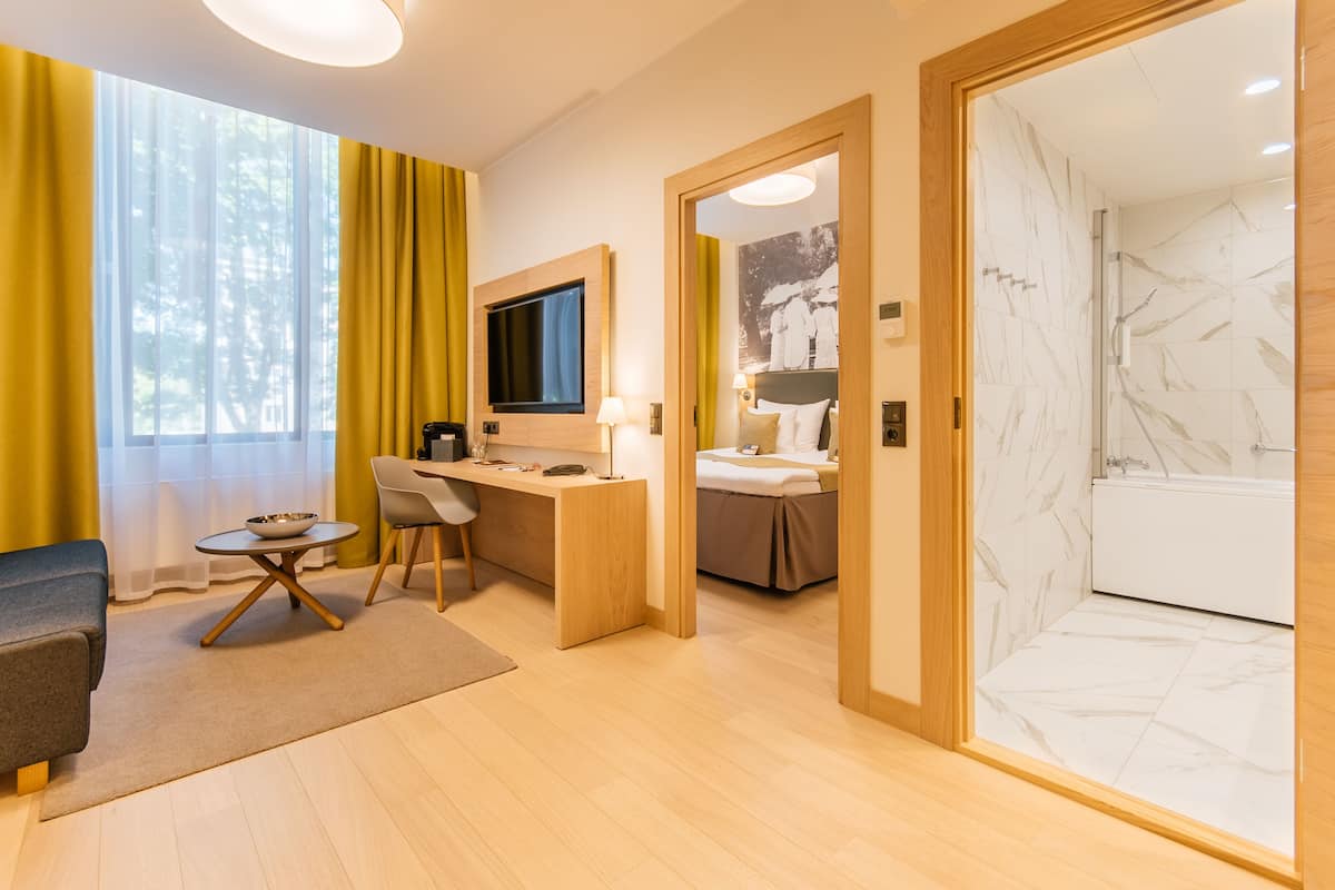 A hotel room with a desk, chair, bed, TV, and a bathroom with marble tiles.