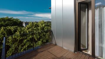A balcony with a wooden floor, a metal railing, and a glass door leading to an interior space.