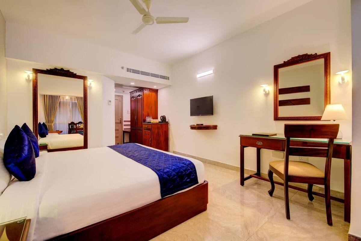 A hotel room with a bed, a desk, a chair, a television, and a mirror.